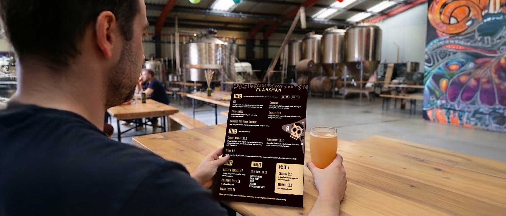 Mock up of a man holding the Flankman menu while holding a pint at the Two by Two Brewery